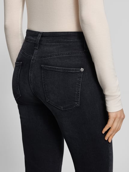 Frauenmodel trägt Slim Fit Jeans mit Label-Patch Modell 'PIPER CROPPED' von CAMBIO, dunkle Denimoptik, Detailaufnahme, KI-modifiziertes Bild.
