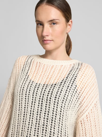Frauenmodel trägt Loose Fit Pullover aus Woll-Mix von BOSS Orange in Creme mit transparenter Strickstruktur, Nahaufnahme Oberkörper.