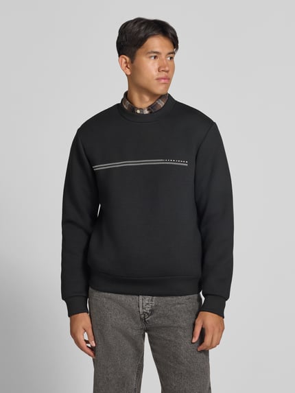 Männermodel trägt Relaxed Fit Sweatshirt mit Viskose-Anteil Modell 'Fusion' von JACK & JONES, Schwarz mit Logo-Print, Ganzkörperansicht von vorne. Herren Sweatshirt, Langarm, elastische Abschlüsse, Größe M: Rückenlänge 66 cm, Ärmellänge 66 cm, Material-Mix, dezenter Stil.