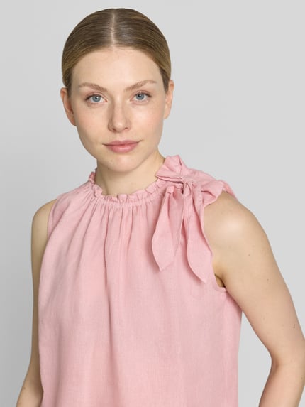 Vrouwenmodel draagt Regular Fit blouse uit viscosemix met linnen van Christian Berg Woman in lichtroze met sierstrik en ruches, mouwloos design, nahaufnahme bovenlichaam. Context: dames blouse van Christian Berg Woman, viscosemix met linnen, regular fit, sierstrik, opstaande kraag met ruches, mouwloos design, ruglengte bij maat 36: 54 cm.