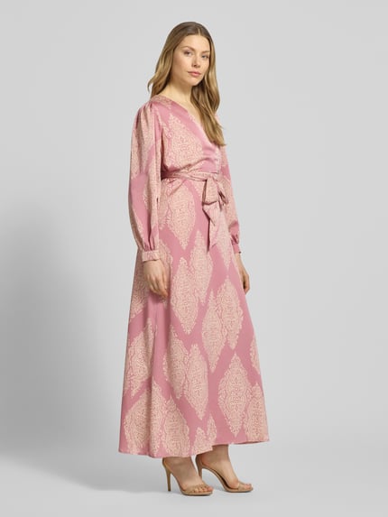 Vrouwenmodel draagt Regular Fit avondjurk met all-over paisleyprint model 'Bretti' van Neo Noir in satijn, met lange mouwen, V-hals, getailleerd, afneembare stoffen band, wikkellook, mouwboord, kleur lichtroze en crème, ruglengte maat 36: 131 cm, borstwijdte 48 cm, mouwlengte 63 cm. Ganzkörperansicht van voren.