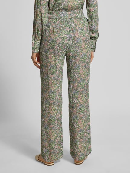 Frauenmodel trägt Stoffhose aus Viskose im Allover-Look Modell 'Bala' von MOS MOSH, grün mit floralen Mustern, elastischer Bund, Ganzkörperansicht Rückansicht.