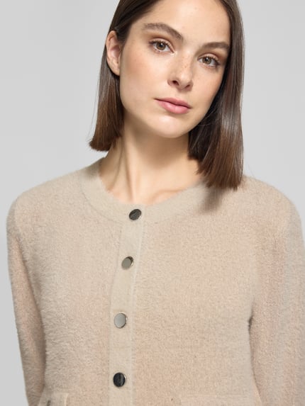 Frauenmodel trägt Strickjacke mit Boucléstruktur von Betty Barclay in unifarbenem Beige mit Zierknöpfen und Pattentaschen, Nahaufnahme Oberkörper.