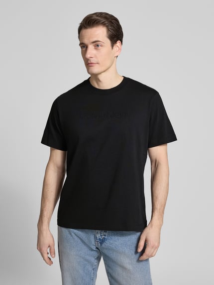 Männermodel trägt T-Shirt mit Rundhalsausschnitt von CK Calvin Klein, schwarze Farbe, Regular-Fit, Logo, Reine Baumwolle, Ganzkörperansicht von vorne. Rückenlänge bei Größe M: 67 cm.