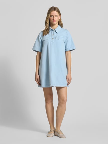 Frauenmodel trägt Oversized Minikleid aus reiner Baumwolle von Tommy Jeans in Optik: Unifarben, Passform: Oversize, Länge: Mini, Ausschnitt: Hochgeschlossen, Applikation: Logo-Stitching, Verschluss: Knopfleiste, Ärmelform: Kurzarm, Material: Reine Baumwolle; Ganzkörperansicht von vorne.