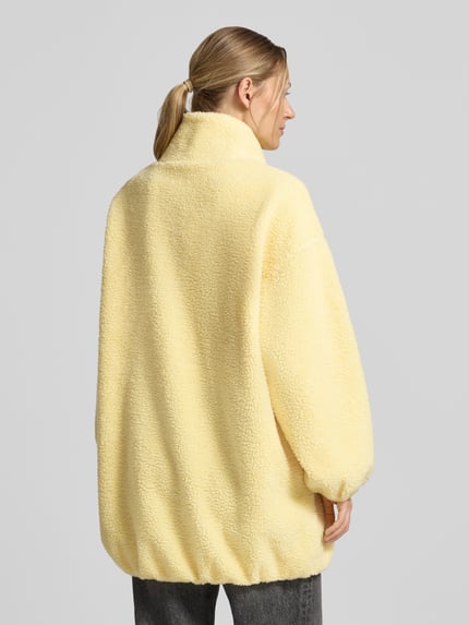 Frauenmodel trägt Oversized Jacke mit Stehkragen Modell 'Hoktown' von American Vintage in Gelb, Fleece-Struktur, Ganzkörperansicht Rückansicht.