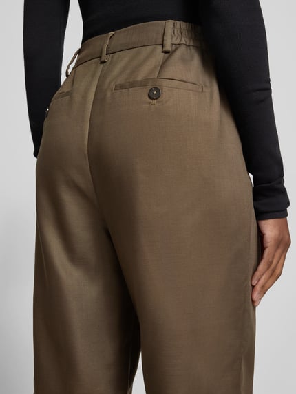 Frauenmodel trägt Straight Fit Chino mit Kellerfalten von black palms in Olivbraun, glatte Oberfläche, Nahaufnahme Rückansicht, Kontext: Damen Chino, Knopf- und Reißverschluss, Eingrifftaschen, Innenbeinlänge 83 cm, Bundweite 39 cm.
