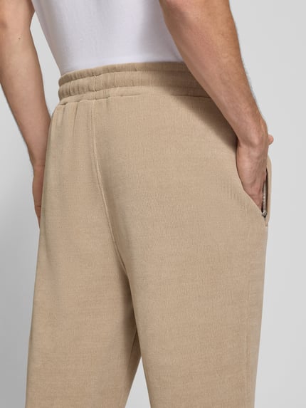 Männermodel trägt Wide Fit Sweatpants mit Label-Detail Modell 'Mezzano' von PEGADOR in Beige, elastischer Bund, Nahaufnahme Rückansicht, elastischer Material-Mix, Eingrifftaschen