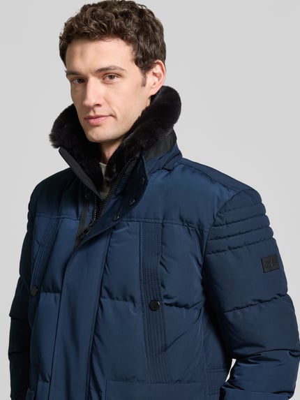 Männermodel trägt Parka mit Kapuze von NAUTGÅRD 'J-LHOTSE 226', unikleurig, lang, labeldetail, sierzak, deelnaden, capuchon, rits, zakken, pas, drukknoopsluiting, klepzakken, ritszakken, binnenzak, lange mouw, elastische mouwsluiting, tunnelkoord, Nahaufnahme Oberkörper.