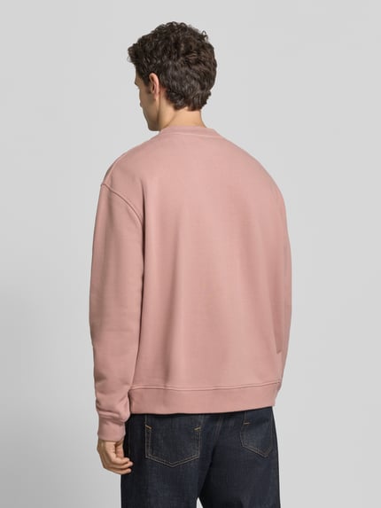 Männermodel trägt Sweatshirt mit Logo-Stitching Modell 'asher crew' von AllSaints, unifarben, Rundhals, gerippte Bündchen, Stricktextur, Ganzkörperansicht Rückansicht.