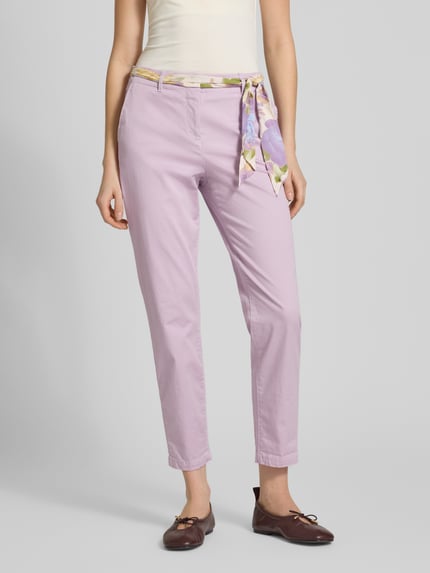 Kobieta prezentuje Slim Fit Chino mit Viskose-Anteil von Christian Berg Woman, jasnofioletowy kolor, mieszanka bawełny i wiskozy, krój slim fit, skrócona długość, materiałowa tasiemka, zapięcie na guzik i zamek błyskawiczny, mieszanka elastycznych materiałów, ujęcie całej sylwetki z przodu.