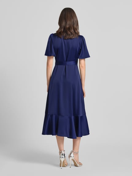 Männermodel trägt Cocktailkleid mit Volantsaum Modell 'THEA' von YAS, satyn, krój taliowany, długość midi, tylny widok całej sylwetki