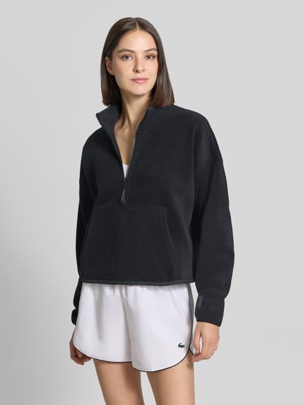 Frauenmodel trägt Relaxed Fit Pullover Troyer-Kragen Modell 'Polar' von Fabletics in Schwarz, Fleece, Kängurutasche, Ganzkörperansicht von vorne.