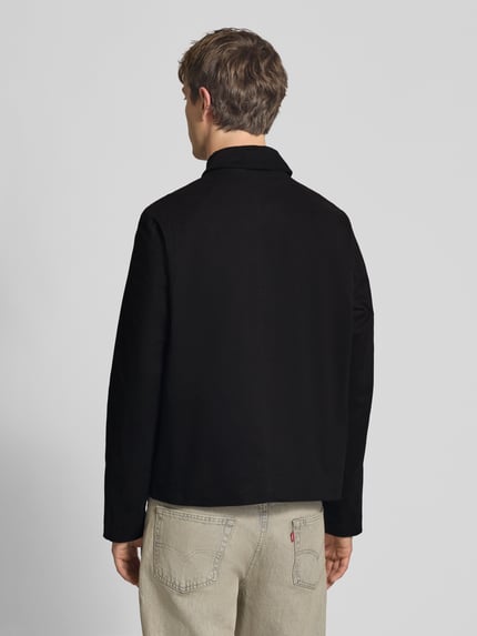 Männermodel trägt Jacke mit Umlegekragen Modell 'GRAHAM' von Jack & Jones, regular fit, knoopsluiting, ruglengte maat M 67 cm, schouderbreedte 40 cm, borstwijdte 58 cm, mouwlengte 73 cm, effen zwart, rechte vormen, gladde structuur. Ganzkörperansicht Rückansicht.