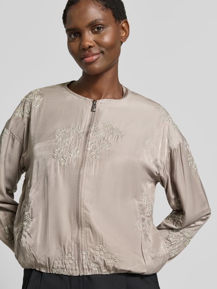 Frauenmodel trägt Blouson aus Viskose-Mix mit Motiv-Stitching Modell 'Ta44mika' von ZABAIONE, beige, Zierperlen, Nahaufnahme Oberkörper.