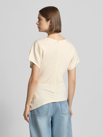 Vrouwenmodel draagt T-shirt met asymmetrisch model 'Maria' van Gina Tricot van viscosemix met structuurpatroon, ronde hals, ruglengte maat S 59 cm, lichtbeige kleur en subtiele textuur, geheel van achteren te zien, Ganzkörperansicht Rückansicht.