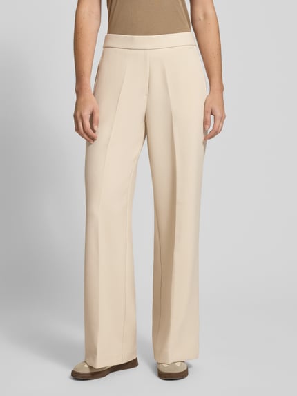 Frauenmodel trägt Wide Fit Stoffhose mit Viskose-Anteil Modell 'Charlie' von Someday, Beige, elastischer Material-Mix, Bügelfalten, Ganzkörperansicht von vorne.