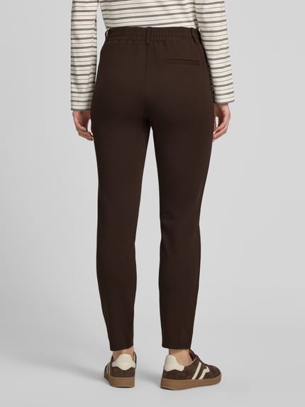 Frauenmodel trägt Loose Fit Bundfaltenhose aus Viskose-Mix von Tom Tailor in Dunkelbraun, glatte Textur, Ganzkörperansicht Rückansicht, Damen Bundfaltenhose.