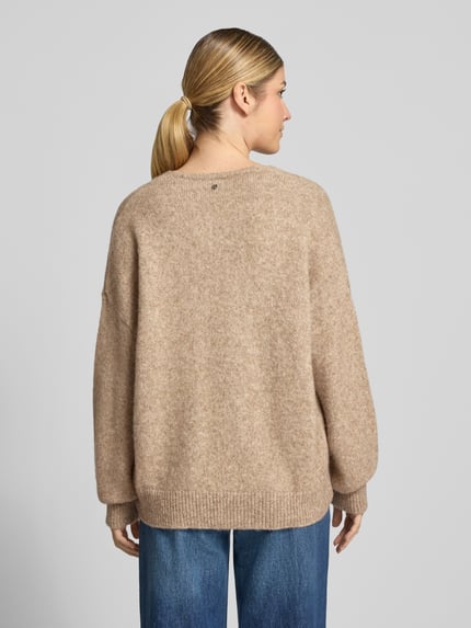 Vrouwenmodel draagt Loose Fit pullover uit alpaca-wolmix Model 'Fondyssa' van BOSS Orange met mêlee en gebreide look, v-hals, lange mouwen met geribde boorden, asymmetrische rompzoom, tricotlook, materiaalverwerking: gebreid, mix van alpaca en wol, geheellichaamsaanzicht achteraan.
