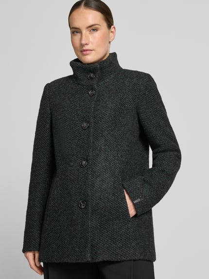Frauenmodel trägt Jacke mit Stehkragen Modell 'JANINE' von Milo Coats, dunkle Farbe, strukturierter Material-Mix, Knopfverschluss, Nahaufnahme Oberkörper. Material: Schurwoll-Anteil, Slim Fit, Eingrifftaschen, Kontext Damen Jacke.
