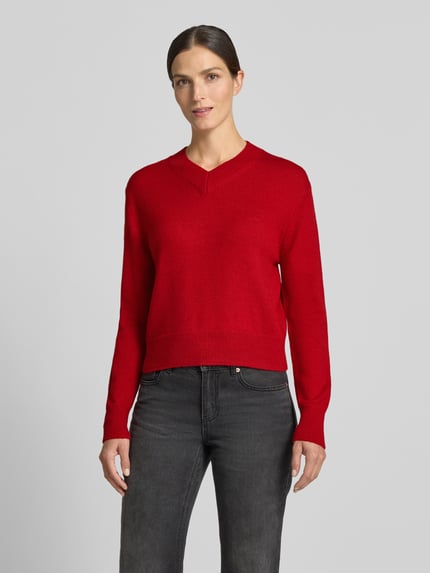 Frauenmodel trägt Strickpullover mit V-Ausschnitt Modell 'LIMONI' von MANGO in kräftigem Rot, Regular Fit, elastische Abschlüsse, Ganzkörperansicht von vorne.
