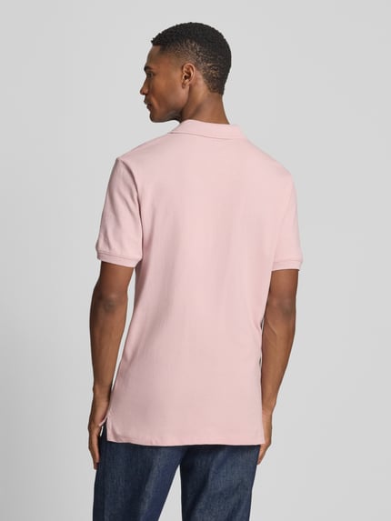 Męski model nosi Slim Fit Poloshirt mit Label-Stitching od GAP, mieszanka bawełny i elastanu, krój slim fit, listwa guzikowa, długość tyłu w rozmiarze M: 70 cm, jasnoróżowa koszulka polo, gładka struktura; widok całej sylwetki z tyłu.