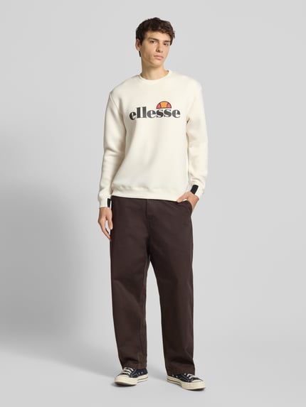 Męski model nosi Sweatshirt mit Label-Print Modell 'CORVARO' od Ellesse, kremowy, luźny krój, żebrowane wykończenia, widok całej sylwetki z przodu.
