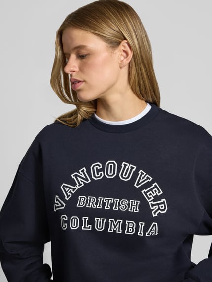 Vrouwenmodel draagt donkerblauw sweatshirt uit katoenmix met statementprint, model 'MERLE' van JIXX, los model, detailopname bovenlichaam.