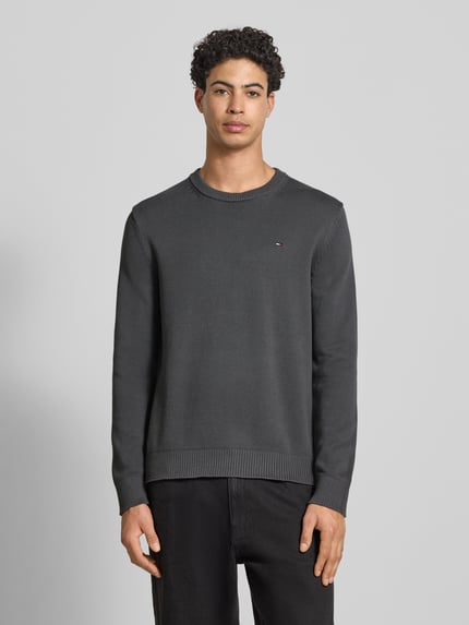 Männermodel trägt Regular Fit Strickpullover aus reiner Baumwolle von Tommy Jeans, unifarben, Rundhals, Logo-Detail, Ganzkörperansicht von vorne.