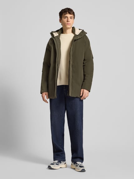 Männermodel trägt olivgrünen Parka mit Kapuze Modell 'WOOD' von Jack & Jones, Regular Fit, verdeckter Reißverschluss, Ganzkörperansicht von vorne.