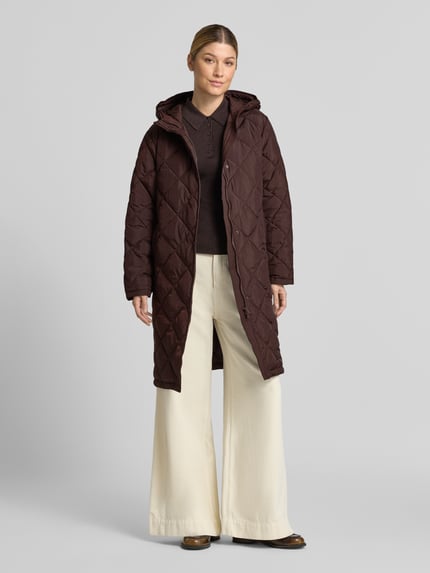 Frauenmodel trägt Steppmantel mit Kapuze Modell 'Olga' von FREE/QUENT in Braun, sichtbare Knopfleiste, Regular Fit, Ganzkörperansicht von vorne. Damen Steppmantel von FREE/QUENT, Rückenlänge 98 cm, Schulterbreite 47 cm, Brustweite 55 cm, Ärmellänge 60 cm.