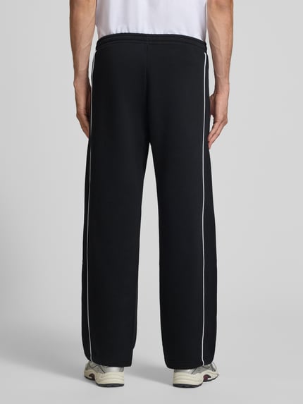 Männermodel trägt Straight Fit Sweatpants aus reiner Baumwolle mit Label-Patch von REVIEW, schwarze Farbe, Ganzkörperansicht Rückansicht. Innenbeinlänge bei Größe M 40 cm, elastischer Bund, seitliche Eingrifftaschen, glatte Textur.
