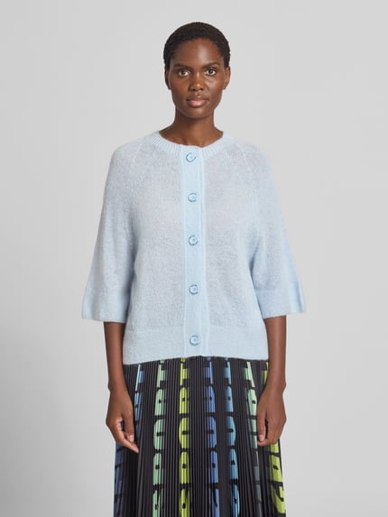 Frauenmodel trägt Wolljacke mit Mohair-Anteil von Marc Cain in Hellblau, lockere Passform, Rundhalsausschnitt, 3/4-Arm, Ganzkörperansicht von vorne.