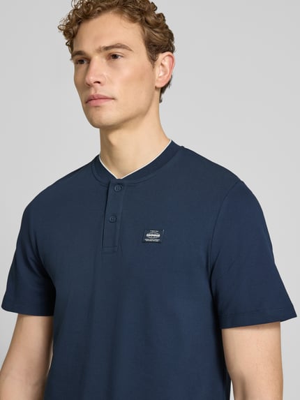 Mannenmodel draagt Regular Fit Poloshirt aus Baumwoll-Mix van s.Oliver RED LABEL in effen donkerblauw, piqué katoenmix, label patch, korte mouw, Henley hals, 2-knoopsluiting, Nahaufnahme bovenlichaam.
