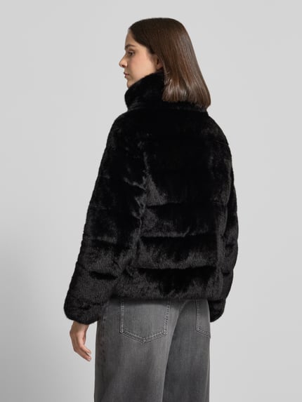 Frauenmodel trägt schwarze glänzende Webpelzjacke mit Struktur und Zweiwege Reißverschluss von S. OLIVER BLACK LABEL, Ganzkörperansicht Rückansicht.