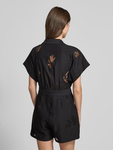 Männermodel trägt kombinezon w stylu kopertowym z haftem angielskim z bawełny, krój relaxed fit, model 'TRACY' od SUNCOO PARIS, kołnierzyk koszulowy, wiązany pasek, czarny kolor, całkowita długość 81 cm, długość wewnętrzna nogawki 11 cm, Ganzkörperansicht Rückansicht.