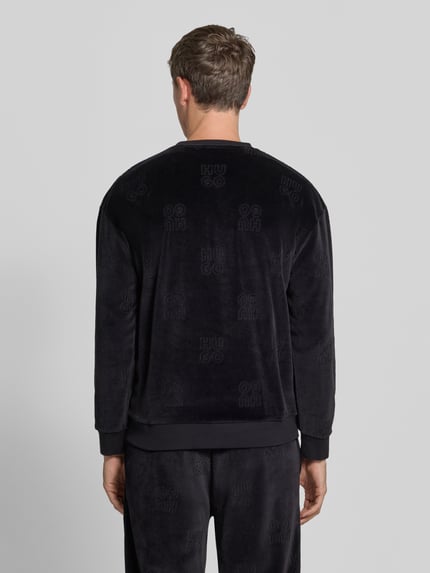Männermodel trägt Sweatshirt mit Samtstruktur von HUGO, schwarz mit Allover-Muster und Struktur, Rundhals, Ganzkörperansicht Rückansicht.