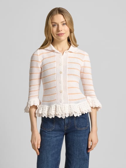 Vrouwenmodel draagt Strickjacke met platte kraag van Rich & Royal, katoenmix, slim fit, gaatjesmotief, rucherand, 3/4-mouw, doorlopende knoopsluiting, ruglengte maat S 54 cm, mouwlengte maat S 42 cm, wit met beige, structuur en textuurmix. Ganzkörperansicht van voren.