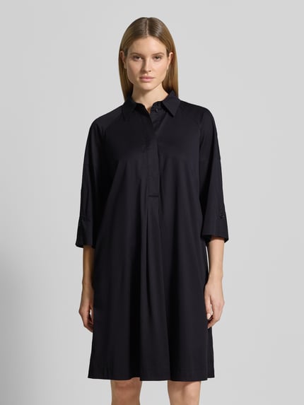 Frauenmodel trägt Hemdblusenkleid mit überschnittenen Schultern von Marc Cain in Schwarz, Baumwolle/Viskose, Gerader-Schnitt, 3/4-Arm, Hemdblusenkragen, verdeckte Knopfleiste, Label-Detail, Ganzkörperansicht von vorne.
