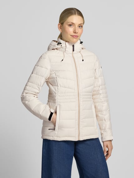 Frauenmodel trägt Jacke mit Kapuze und Label-Patch Modell von G.I.G.A. DX in hellem Beige mit Steppstruktur, Ganzkörperansicht von vorne.