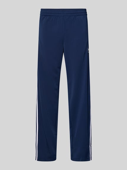 Produktfoto, Trainingshose mit Kontraststreifen und Reißverschlusstaschen od adidas Originals, krój regular fit, elastyczny pas, model FIREBIRD, granatowy kolor, białe paski, wyhaftowane logo, kieszenie zapinane na zamek błyskawiczny, długość wewnętrzna nogawki 78 cm dla rozmiaru M.