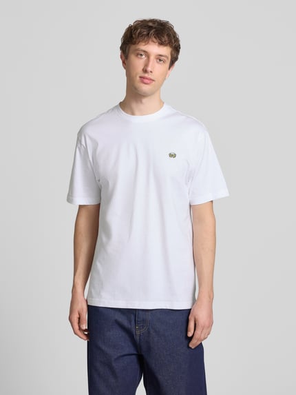 Männermodel trägt Relaxed Fit T-Shirt aus reiner Baumwolle Modell 'FRED' von Only & Sons, unifarben weiß, kurzarm, Rundhals, Jersey, Motiv-Stitching, Label Patch, Ganzkörperansicht von vorne.