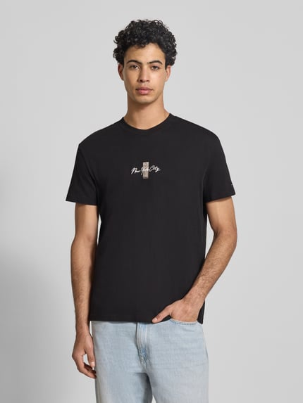Männermodel trägt Regular Fit T-Shirt aus reiner Baumwolle Modell 'SIGN BLOCK' von Tommy Jeans, Optik: Unifarben, Kurzarmpassform, Schriftzug-Stitching, Label Print, Rücken-Print, Rundhals, Ganzkörperansicht von vorne.
