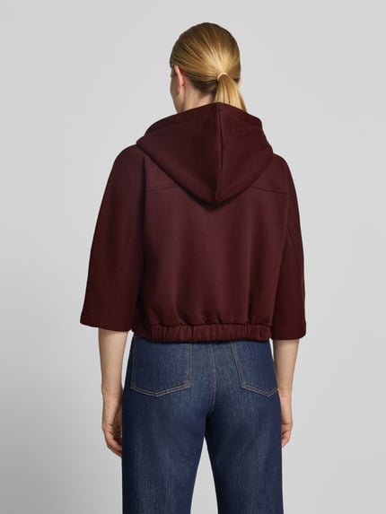 Frauenmodel trägt bordeauxrote Loose Fit Sweatjacke aus Baumwoll-Mix Modell 'Giela' von OPUS, glatte Textur, Ganzkörperansicht Rückansicht. Damen Sweatjacke von OPUS.