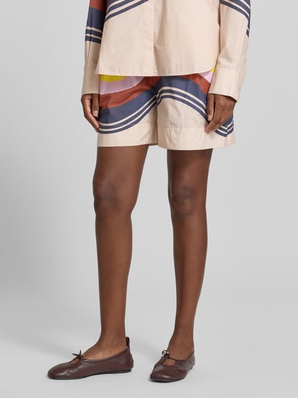 Kobieta nosi Regular Fit Chinoshorts aus reiner Baumwolle von Essentiel Antwerp, wzór w wielokolorowe fale, zbliżenie na nogi.