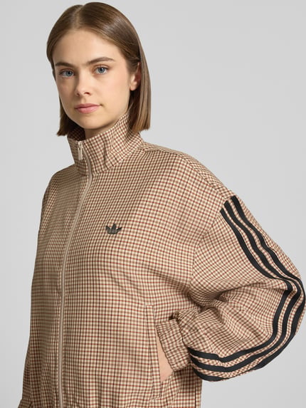 Vrouwenmodel draagt beige-bruine slim fit sweatjack met ruitpatroon en zwart gestikt logo, adidas Originals, Nahaufnahme Oberkörper