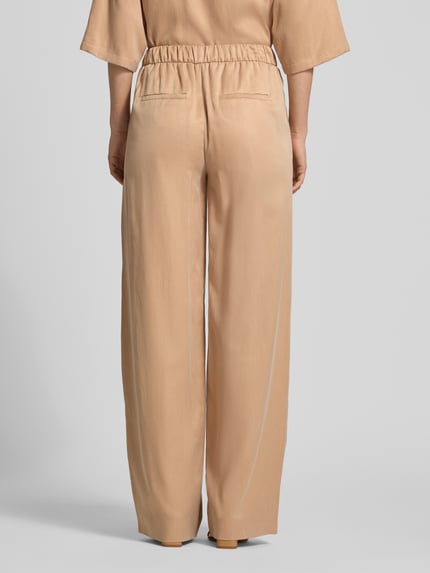 Frauenmodel trägt Wide Fit Stoffhose mit elastischem Bund Modell 'Consider' von Drykorn in Beige, Cupro-Mix, Ganzkörperansicht Rückansicht.