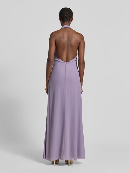 Frauenmodel trägt Abendkleid mit Neckholder von Mascara in Flieder, Chiffon, körpernah, Maxilänge, Rückenansicht, Ganzkörperansicht Rückansicht.