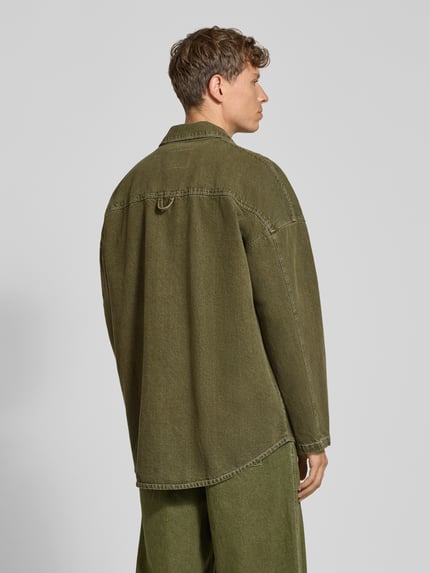 Männermodel trägt Relaxed Fit Jeanshemd mit Label-Detail Modell 'UZATOWN CHEMISES' von American Vintage in Olivgrün, Struktur reine Baumwolle, Brusttaschen, Rückenpartie sichtbar, Ganzkörperansicht Rückansicht.