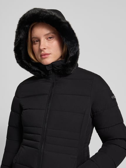 Frauenmodel trägt schwarzen Steppmantel mit Kunstfell-Kapuze, Zweiwege-Reißverschluss, Modell 'ECLIPSE' von NAUTGÅRD, Nahaufnahme Oberkörper. Slim Fit, Damen Steppmantel, Größe S: Rückenlänge 115 cm, Schulterbreite 40 cm, Brustweite 46 cm, Ärmellänge 65 cm.